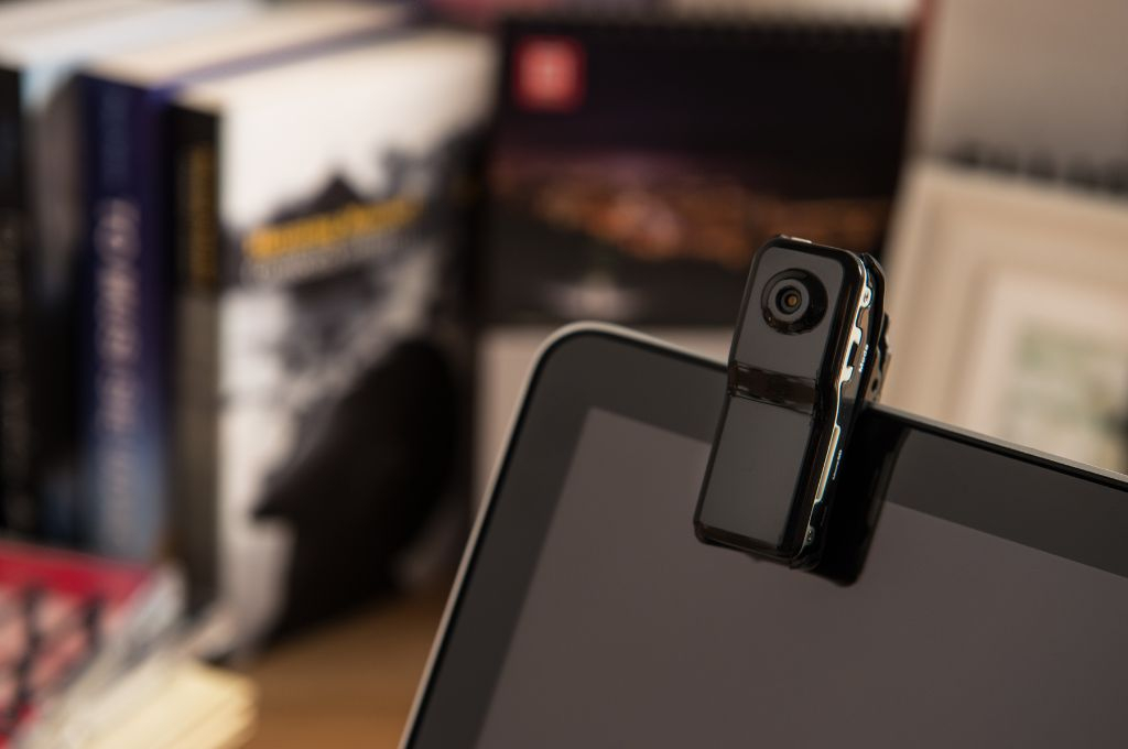 Mini kamery ukryte ciężko dostrzec gołym okiem Alt: Mini kamera zamontowana na górnej krawędzi monitora w domowym biurze, w tle książki.